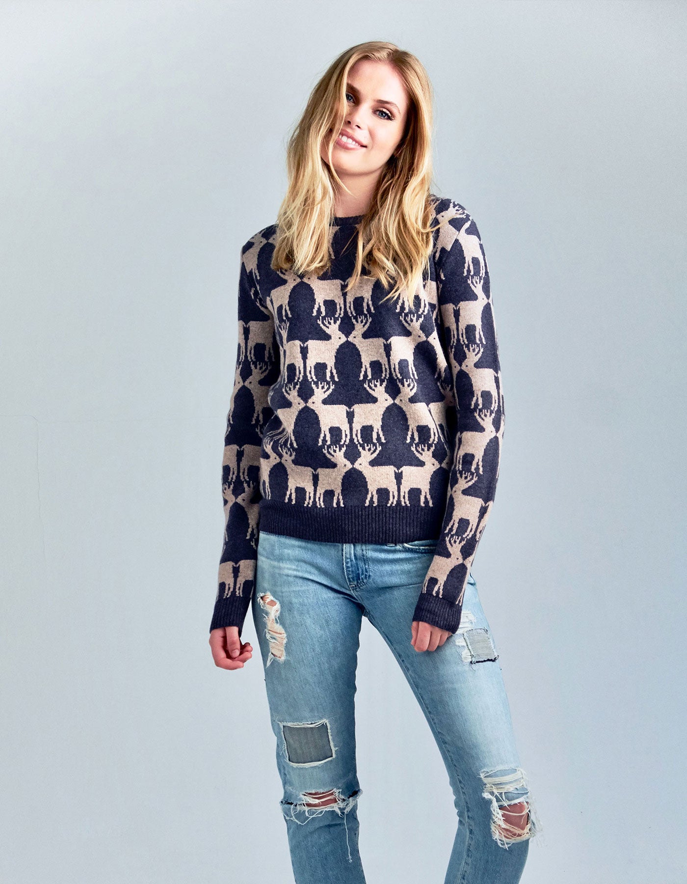 A woman wearing ripped jeans and a reindeer design cashmere jumper.