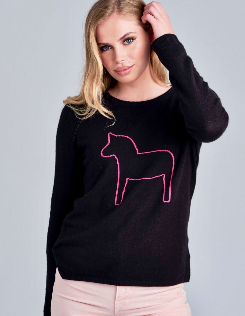A woman modelling a designer cashmere Dalahast jumper, the malin darlin Pony in black with pink design.