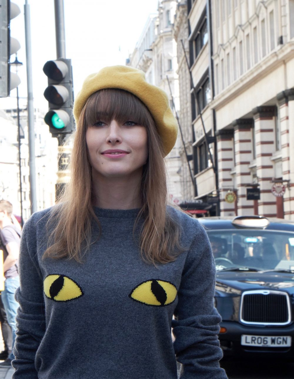 Woman on a busy London street, wearing a cashmere jumper with cat eyes knitted into the design.