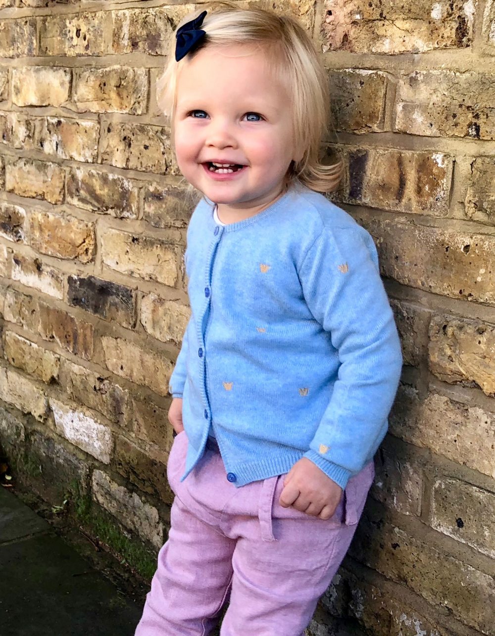 A smiling girl dressed in kids designer cashmere, the malin darlin Baby Cardigan.