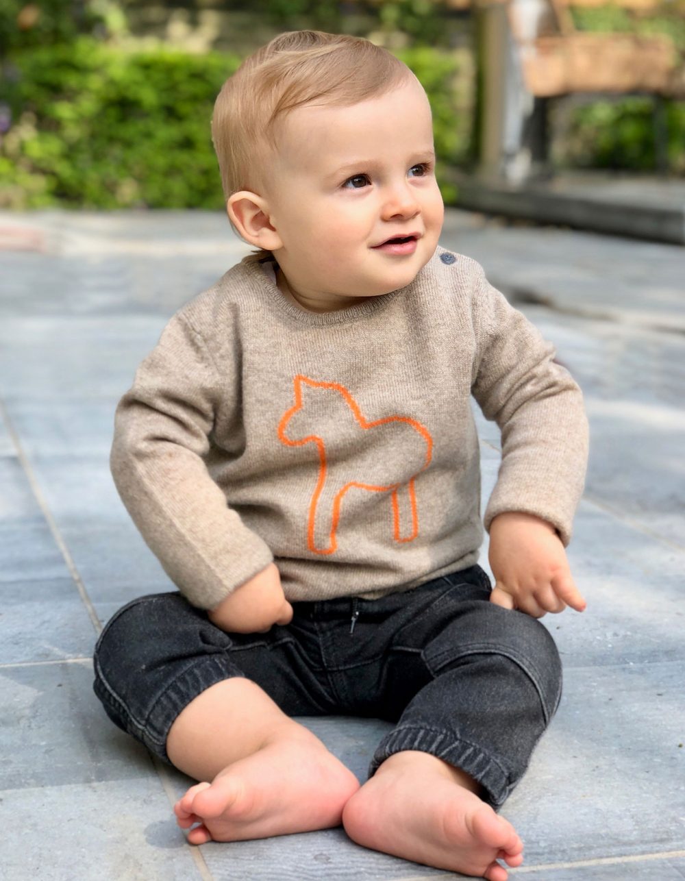 A smiling child wearing the malin darlin Baby Pony beige kids cashmere jumper with washed black jeans.