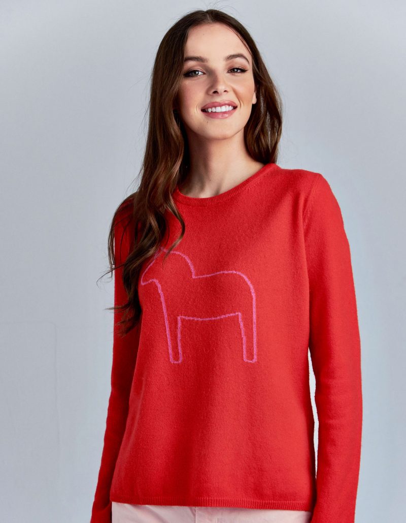 An image of a smiling woman in one of the malin darlin Dalahast horse cashmere jumpers, a pony depicted on red cashmere.