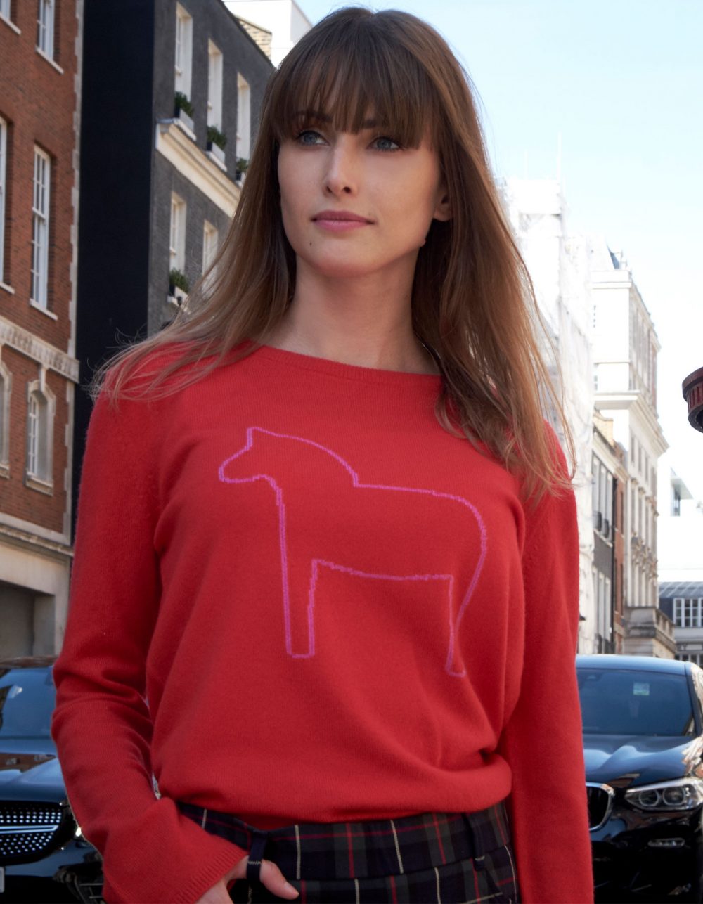 Woman on a street, promoting malin darlin Dalahast horse cashmere jumpers, a pony shown on red cashmere.