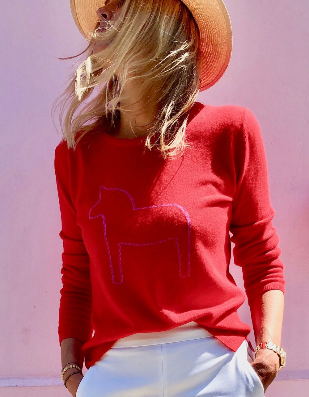 Model wearing malin darlin Dalahast horse cashmere jumpers, a pony shown on red cashmere.