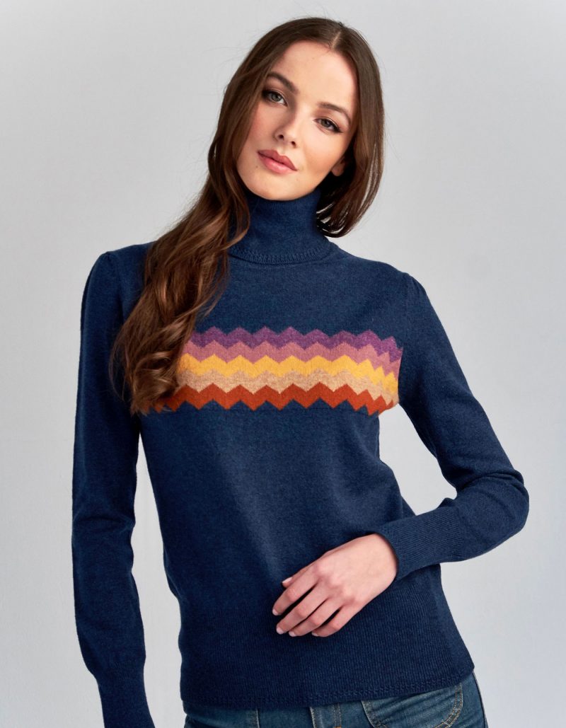 A woman modelling a blue cashmere jumper with zigzag patterning across the front.