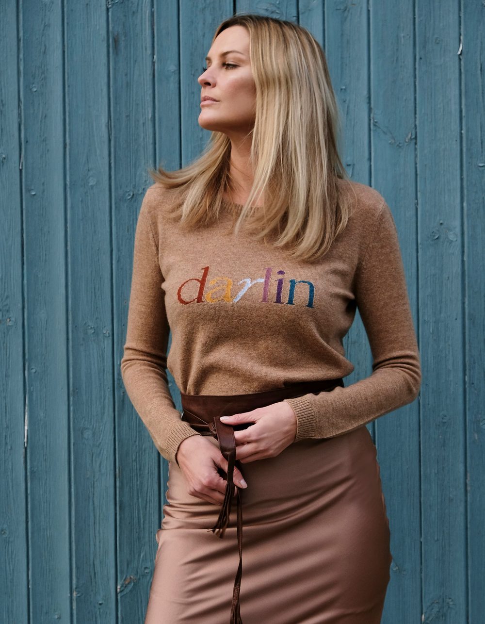 Model in the Darlin Beige cashmere jumper against a wood panel background to show sustainable womens cashmere.