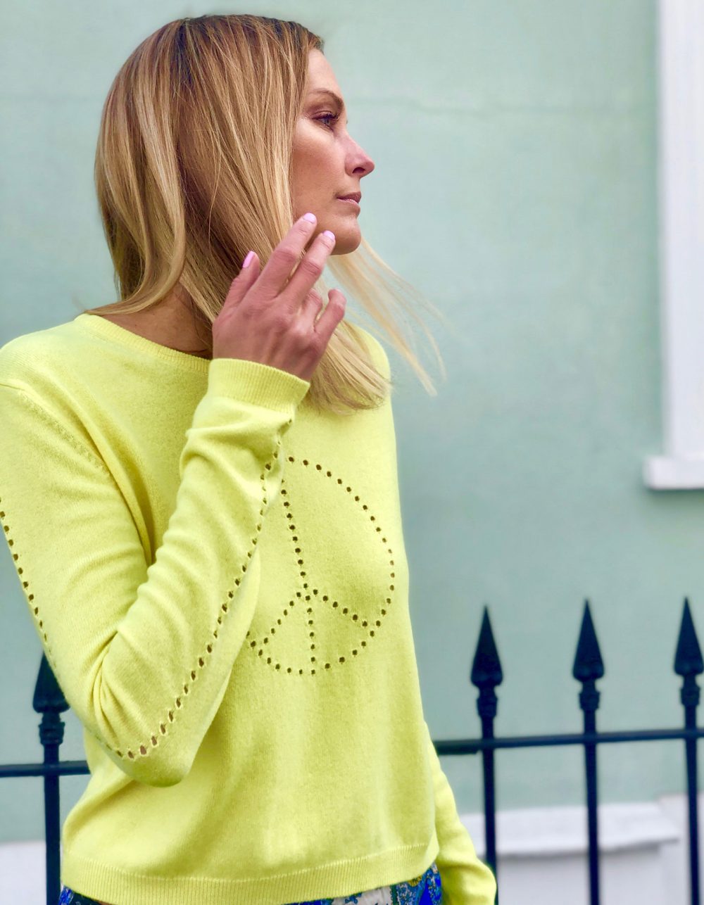 Picture of a model standing by railings in designer cashmere knitwear, the yellow malin darlin Peace cashmere jumper.